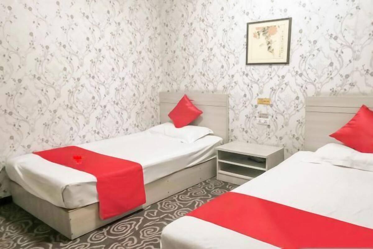 Hotelkamer met twee bedden, elk met een rood kussen, een klein nachtkastje en een lichtschakelaar aan de muur.