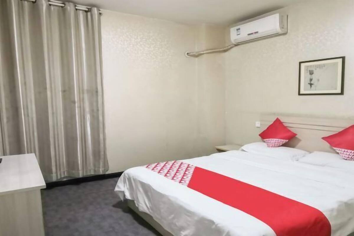 Hotelkamer met een bed, nachtkastje, bureau, stoel, raam met gordijnen, airconditioning en een lijst aan de muur.