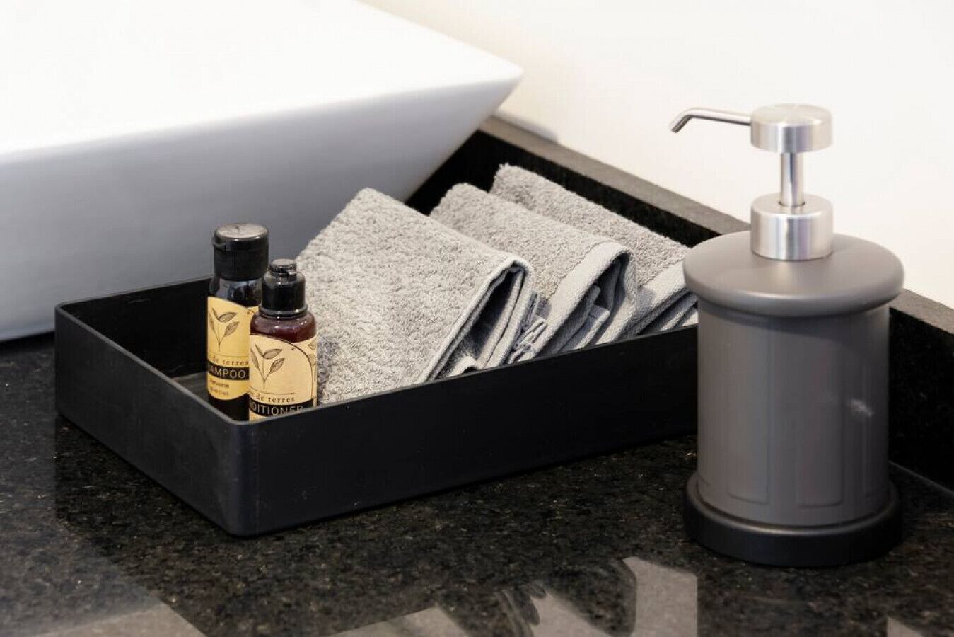 A black storage box containing a bottle of shampoo, a bottle of conditioner, and folded towels.