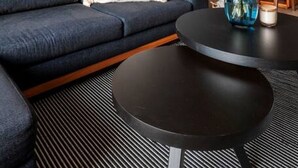 A modern living room with a dark blue sofa, a round black coffee table, and a vase with green plants. There are framed artworks on the wall and a round mirror above the coffee table. - Enjoy skyline/city views from this 17th floor flat (Ciudad de México)