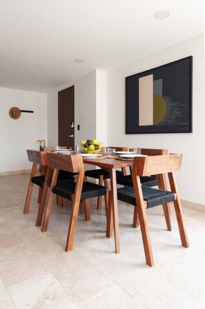 Un coin repas avec une table et des chaises en bois, un panier de fruits sur la table et un tableau au mur.