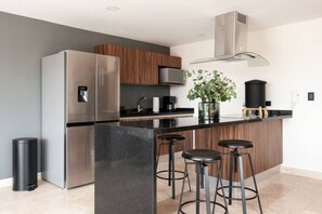 A modern kitchen with a stainless steel refrigerator, a built-in oven, a coffee machine, and a large island with bar stools. - Lux large top floor Apt. at The Corner Condesa (Ciudad de México)