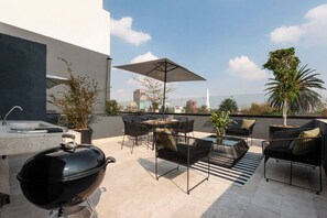 An outdoor patio with a grill, seating area, and a view of the city skyline. - Lux large top floor Apt. at The Corner Condesa (Ciudad de México)