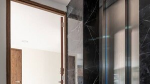 A hallway with a wooden door leading to a room, a glass elevator, and marble flooring. - Lux large top floor Apt. at The Corner Condesa (Ciudad de México)