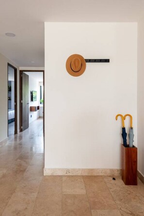 Un couloir avec une porte en bois, un crochet fixé au mur et un banc en bois sur lequel sont posés des parapluies.