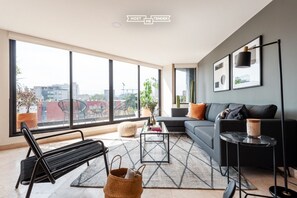 A modern living room with a sofa, coffee table, and a large window offering a city view. - Lux large top floor Apt. at The Corner Condesa (Ciudad de México)