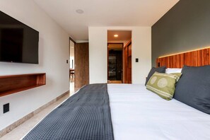 A modern hotel room with a large bed, a flat-screen TV mounted on the wall, and a wooden headboard. - Lux large top floor Apt. at The Corner Condesa (Ciudad de México)