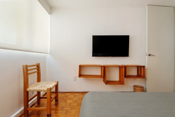 Une chambre à coucher avec un lit, une chaise en bois, un téléviseur fixé au mur et une porte.