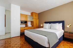 A bedroom with a bed, wooden wardrobe, bedside lamp, and a door leading to another room. - Mayan Sparrow, Stylish Apartment in Casa Quetzal (Ciudad de México)