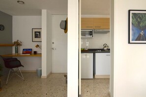 Ein kompakter Wohnbereich mit Küchenzeile, einem Essbereich mit Laptop und einer Blumenvase, und einer Tür, an der ein Hut hängt.