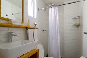 A bathroom with a white sink, a mirror, a towel rack, a shower curtain, and a small shelf with toiletries. - Mayan Sparrow, Stylish Apartment in Casa Quetzal (Ciudad de México)