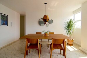 A dining area with a wooden table, four chairs, a hanging light fixture, and a potted plant. - Mayan Sparrow, Stylish Apartment in Casa Quetzal (Ciudad de México)