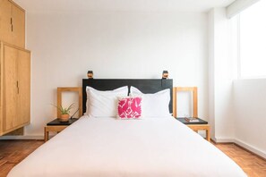 A neatly made bed with white and pink pillows, wooden headboard, and nightstands with a plant and books.