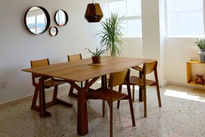 Un coin repas avec une table et des chaises en bois, une plante en pot et une petite étagère ornée d’objets décoratifs.