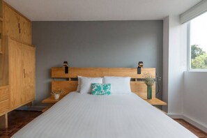 Ein Schlafzimmer mit einem Holz-Kopfteil, weißer Bettwäsche und einem Nachttisch mit einer Vase.