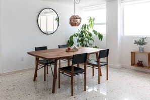 Ein Essbereich mit Holztisch und schwarzen Stühlen, einem runden Spiegel an der Wand, einer Pendelleuchte und einem Blumentopf.