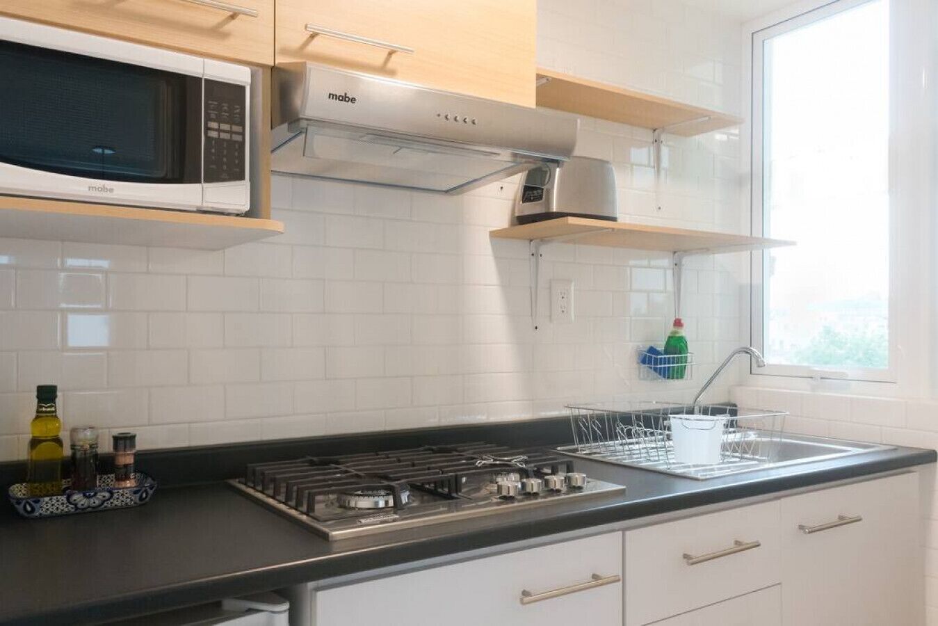 Een moderne keuken met witte kasten, een fornuis, een magnetron en een raam dat natuurlijk licht binnenlaat.