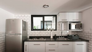 A modern kitchen with white cabinets, a stainless steel refrigerator, a gas stove, a microwave, and a window with a view of greenery outside. - Modern, Industrial Apartment with Bamboo Garden and Rooftop Terrace (Ciudad de México)