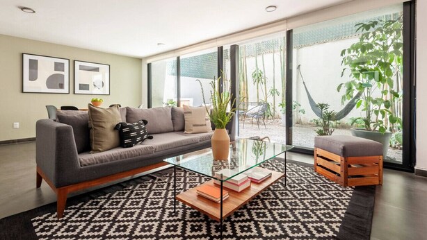 A modern living room with a grey sofa, a glass coffee table, and a patterned rug. - Modern, Industrial Apartment with Bamboo Garden and Rooftop Terrace (Ciudad de México)