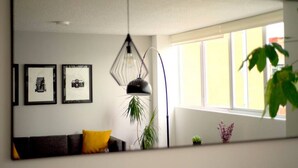A living room with a sofa, two framed pictures, a hanging light fixture, and a window with plants. - Bohemian Rooster, New! Deluxe Apt. in Casa Quetzal (Ciudad de México)
