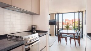 Une cuisine moderne équipée d’une cuisinière à gaz, d’un four et d’une machine à café, qui donne sur un coin repas avec une table et des chaises.