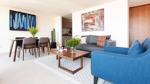 Un salon moderne avec un canapé bleu, un coin repas comprenant des chaises et une table, et une cuisine en arrière-plan.