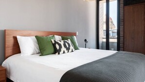 Une chambre d’hôtel moderne avec un grand lit, une tête de lit en bois et une vue sur la ville grâce à une grande fenêtre.