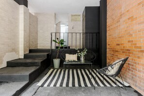 A staircase leading to a landing with a black metal railing, a black and white striped rug, a black metal bench, a potted plant, and a brick wall. - Mandarine Cardinal, Modern Apt. in Casa Quetzal (Ciudad de México)