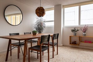 A dining area with a wooden table, six chairs, a hanging light fixture, a large mirror, and a window with a view. - Mandarine Cardinal, Modern Apt. in Casa Quetzal (Ciudad de México)