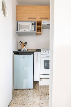A compact kitchen with a refrigerator, oven, microwave, and wooden cabinets. - Mandarine Cardinal, Modern Apt. in Casa Quetzal (Ciudad de México)