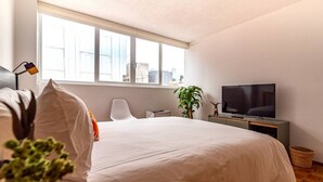 Ein modernes Schlafzimmer mit einem großen Bett, einem Fernseher, einem Schreibtisch und einem Fenster.
