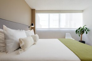 Une chambre d’hôtel avec un lit, une lampe de chevet, une fenêtre et une plante en pot.