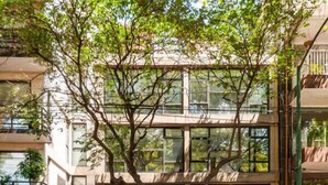 Un edificio moderno con un albero davanti e una bicicletta parcheggiata all'esterno, mentre una persona cammina.