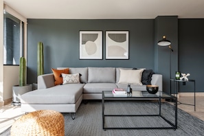 A modern living room with a grey sectional sofa, a glass coffee table, and a cactus plant.