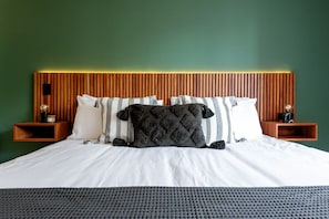 Un lit avec une literie blanche, un plaid gris foncé et des coussins à rayures, le tout placé devant un mur vert.