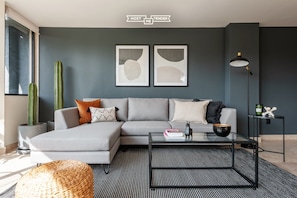 A modern living room with a grey sectional sofa, a glass coffee table, and a cactus plant.