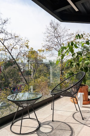 A balcony with two chairs and a table, overlooking a cityscape with trees and buildings.