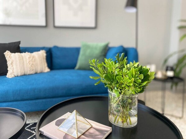 A living room with a blue sofa, a coffee table with a vase of green plants, and framed pictures on the wall. - The Mystique Owl, amazing flat @ Casa Quetzal (Ciudad de México)