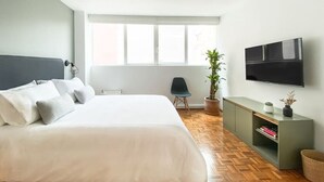 Ein modernes Schlafzimmer mit einem großen Bett, einem an der Wand montierten Fernseher, einer Topfpflanze und Holzboden.