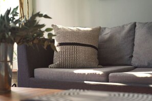 Ein graues Sofa mit einem gemusterten Kissen und einer dunkel gefärbten Vase mit grünen Blättern.