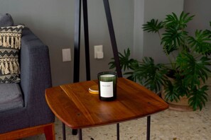 Una habitación con un sofá gris, una pequeña mesa de madera con una vela etiquetada como “WILD MINT” y una planta en maceta.
