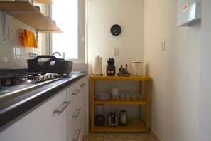 A compact kitchen with white cabinets, a black kettle, a coffee maker, and a shelf with glassware.