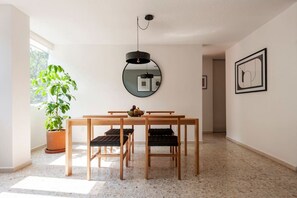 A dining area with a wooden table and chairs, a potted plant, a round mirror, and a framed picture on the wall.
