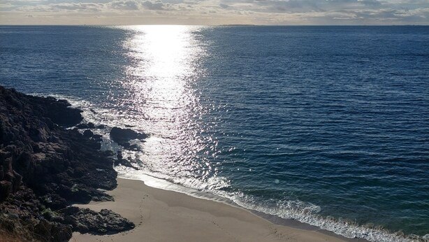 Een strand met heldere lucht en zonlicht dat op het water reflecteert.