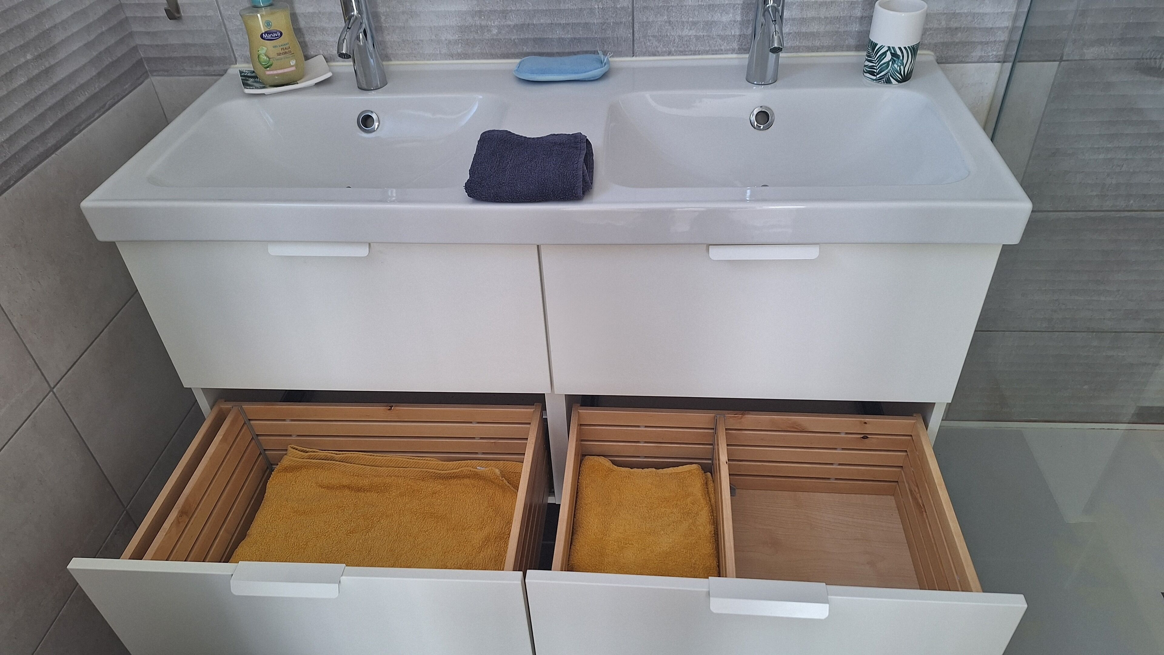 A bathroom with two sinks, a towel rack, and a storage drawer with towels.