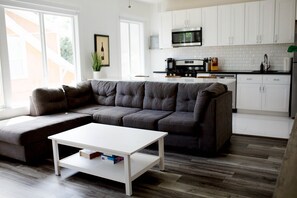 A modern living room with a sectional sofa, a white coffee table, and a kitchen in the background.