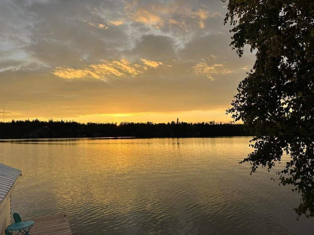 Een rustig meer bij zonsondergang, met een steiger en stoelen.