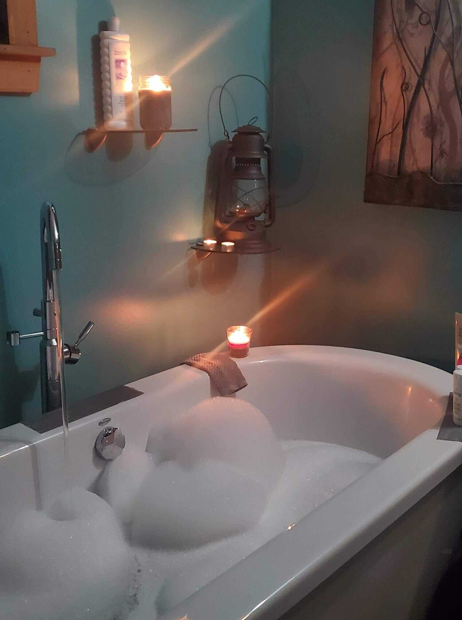 A bathtub with bubbles, a candle, and a wall-mounted heater.