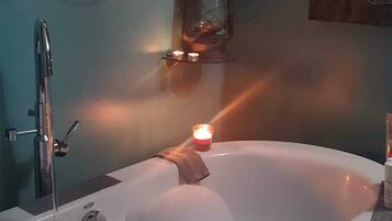 A bathtub with bubbles, a candle, and a wall-mounted heater.