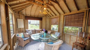 A cozy room with a wooden ceiling, a glass table surrounded by wicker chairs, and a chandelier. - Beautiful All Season Cottage on Remi Lake (Moonbeam)